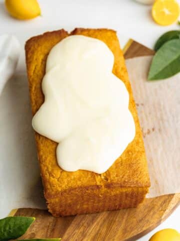 Vegan lemon loaf on a piece of crumpled parchment with the lemon glaze pooling a bit at the bottom.