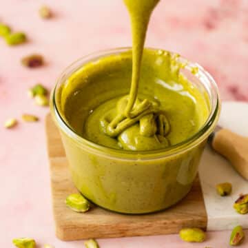 pistachio butter in a glass jar with some drizzling on top showing the smooth, runny, glossy consistency.