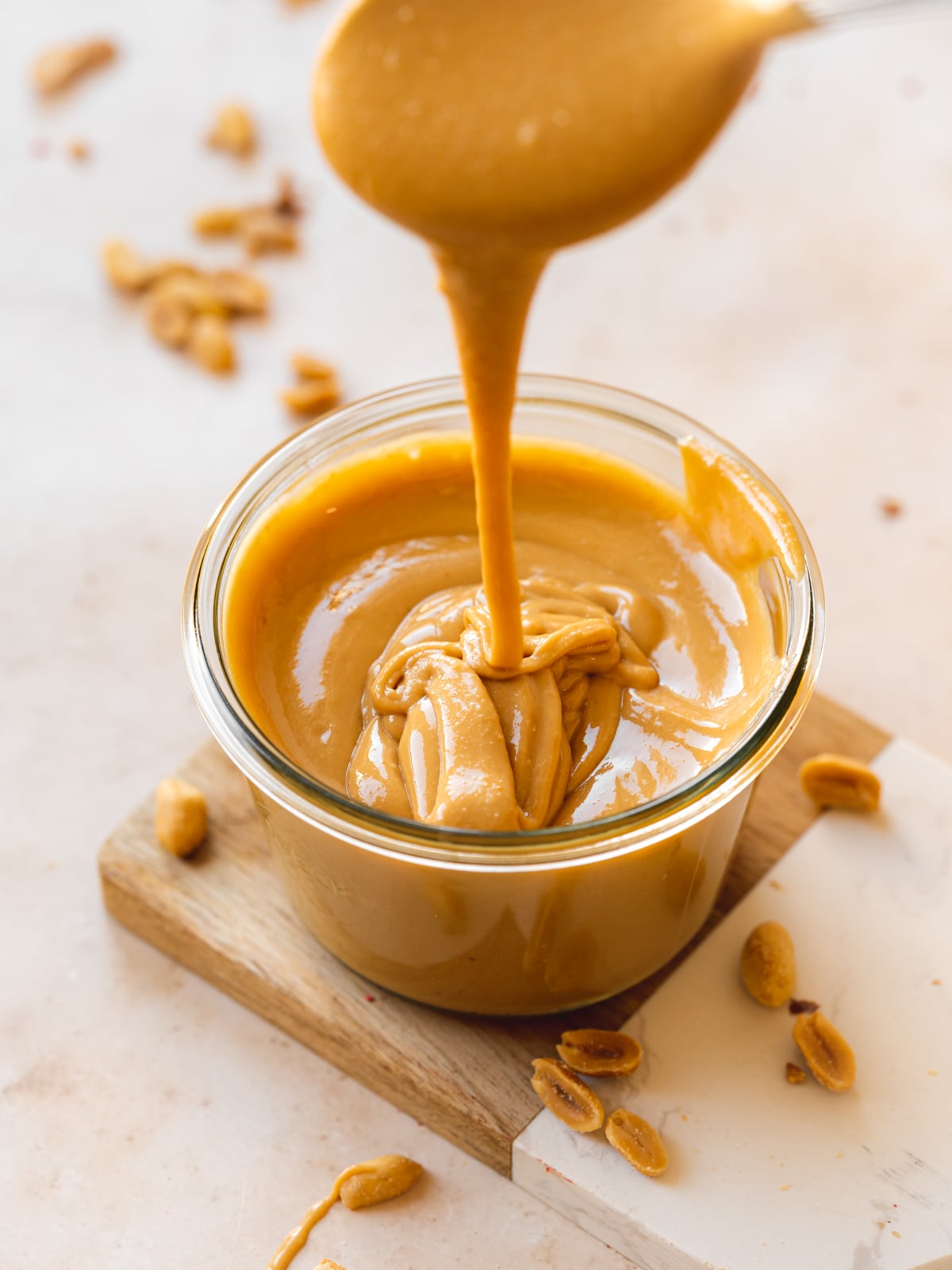peanut butter in a small jar with a spoon drizzling some showing the runny consistency.