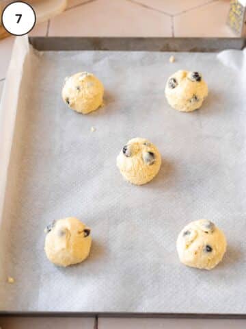 Rounded balls of blueberry lemon cookie dough on a parchment-lined baking sheet.