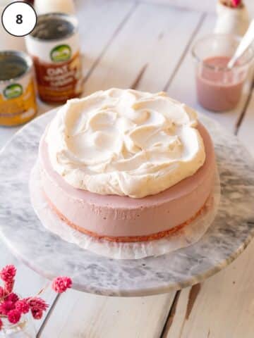 pink vegan cheesecake with whipped cream topping on a marble surface.