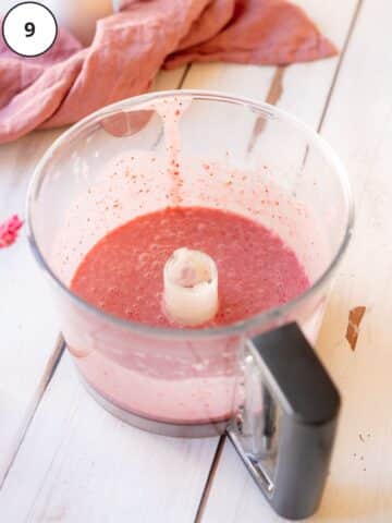 pink strawberry sauce in a food processor jug on a white wooden surface.
