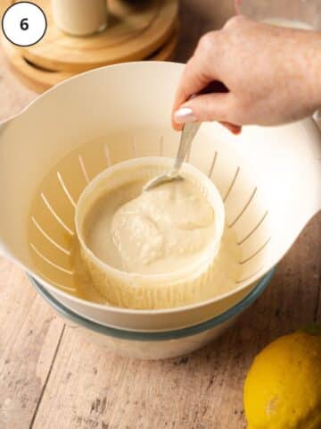 cashew ricotta cheese being stirred in a cheese making mold on top of a colander.