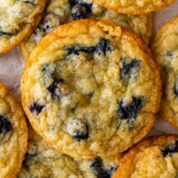 closeup overhead shot of vegan lemon blueberry cookies in a pile. The edges of the cookies are golden brown and crisp, whereas the center of the cookies look soft.