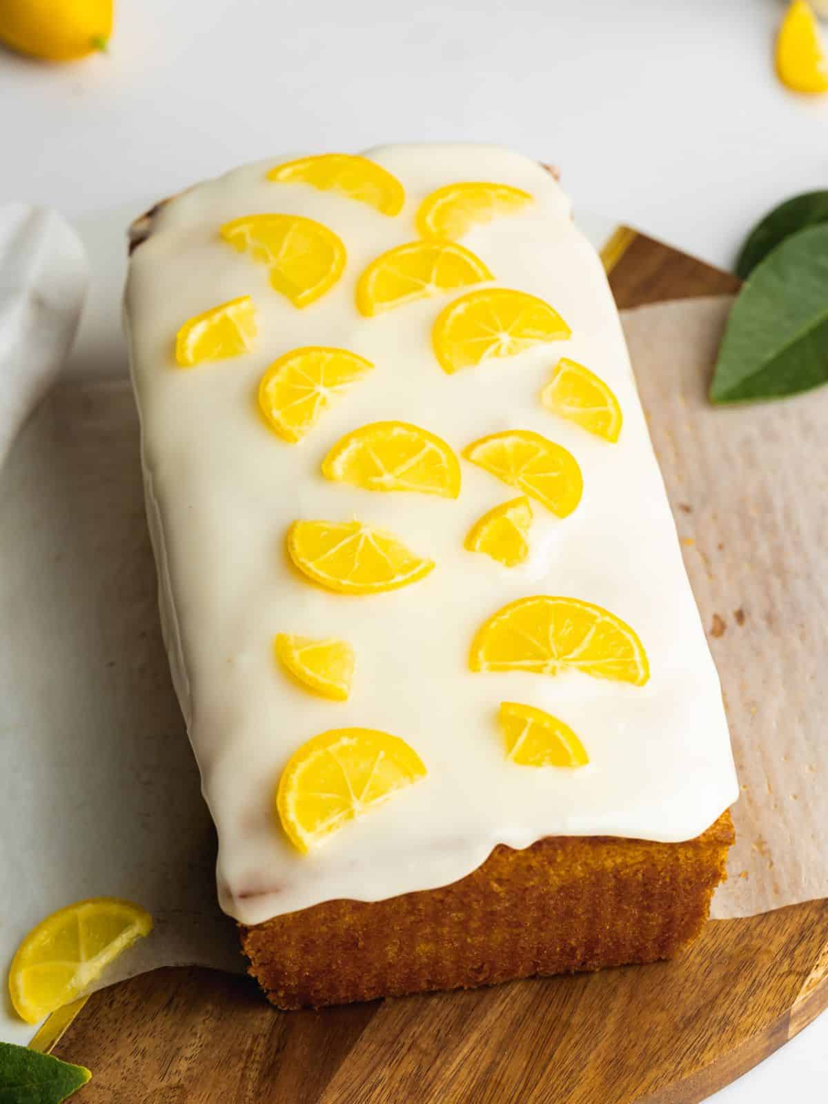 Vegan lemon loaf topped with small lemon slices on a piece of crumpled parchment with the lemon glaze pooling a bit at the bottom.