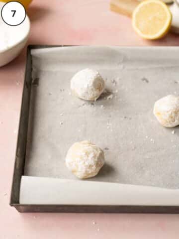 lemon cookie dough balls coated in powdered sugar on a baking sheet lined with parchment paper.