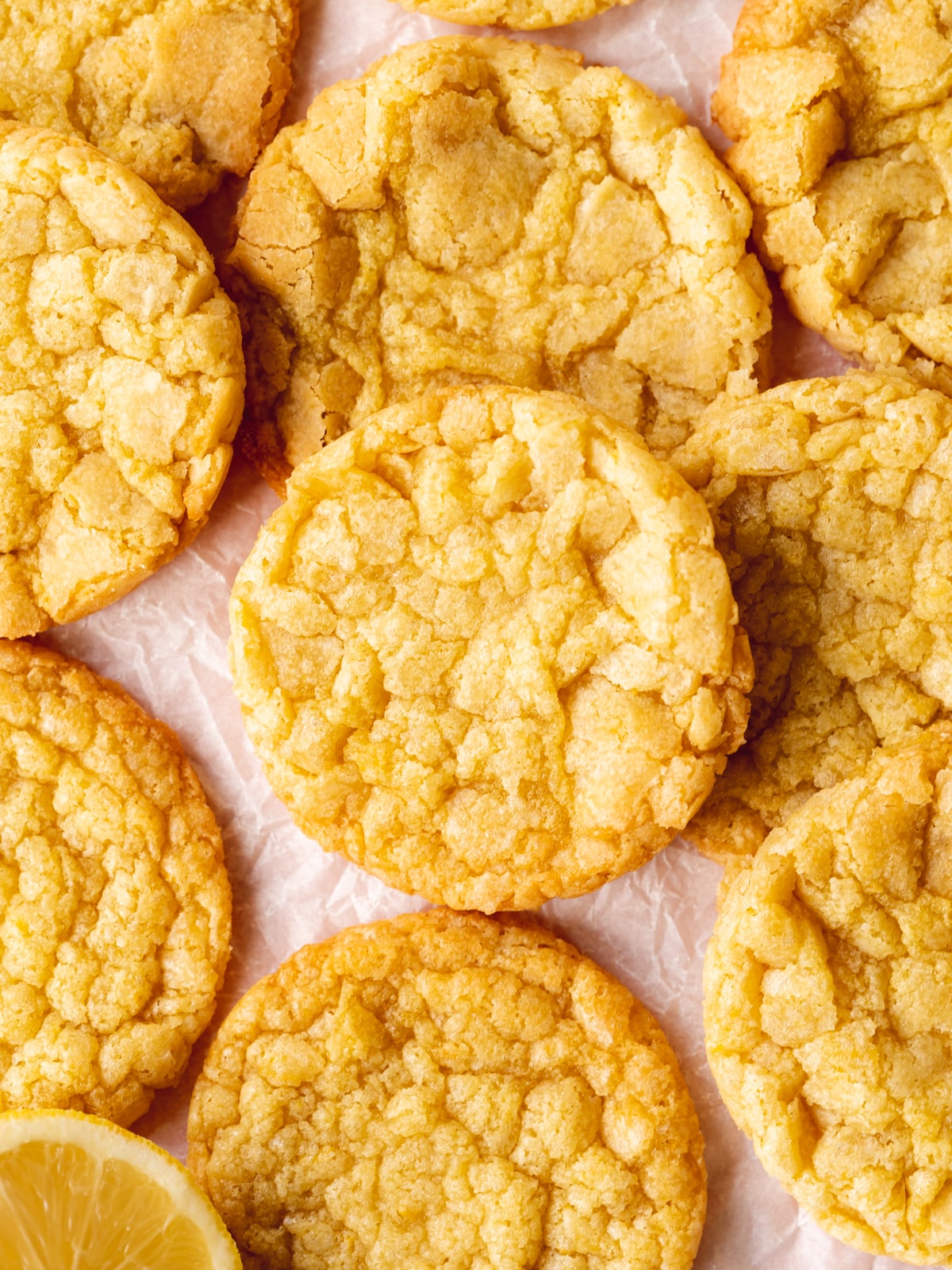 vegan lemon cookies with a crinkle surface laid out on crunched up baking paper with a sliced open lemon on the side.
