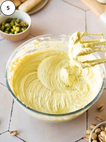 pistachio mascarpone filling for tiramisu whipped in a large nixing bowl, with a whisk showing the creamy consistency.