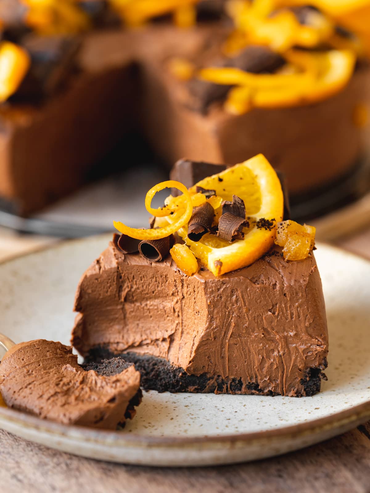Slice of no-bake vegan chocolate orange cheesecake on a speckled plate with a gold fork taking a bite out of it.