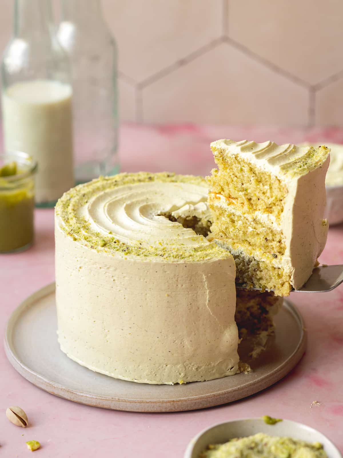 vegan pistachio cake with a slice being lifted out of it with a cake slice on a ceramic plate.