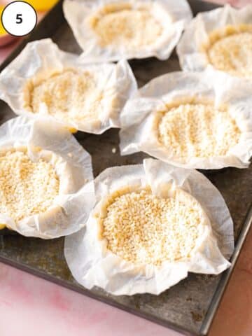 Tart shells are lined with parchment and filled with rice for blind baking.