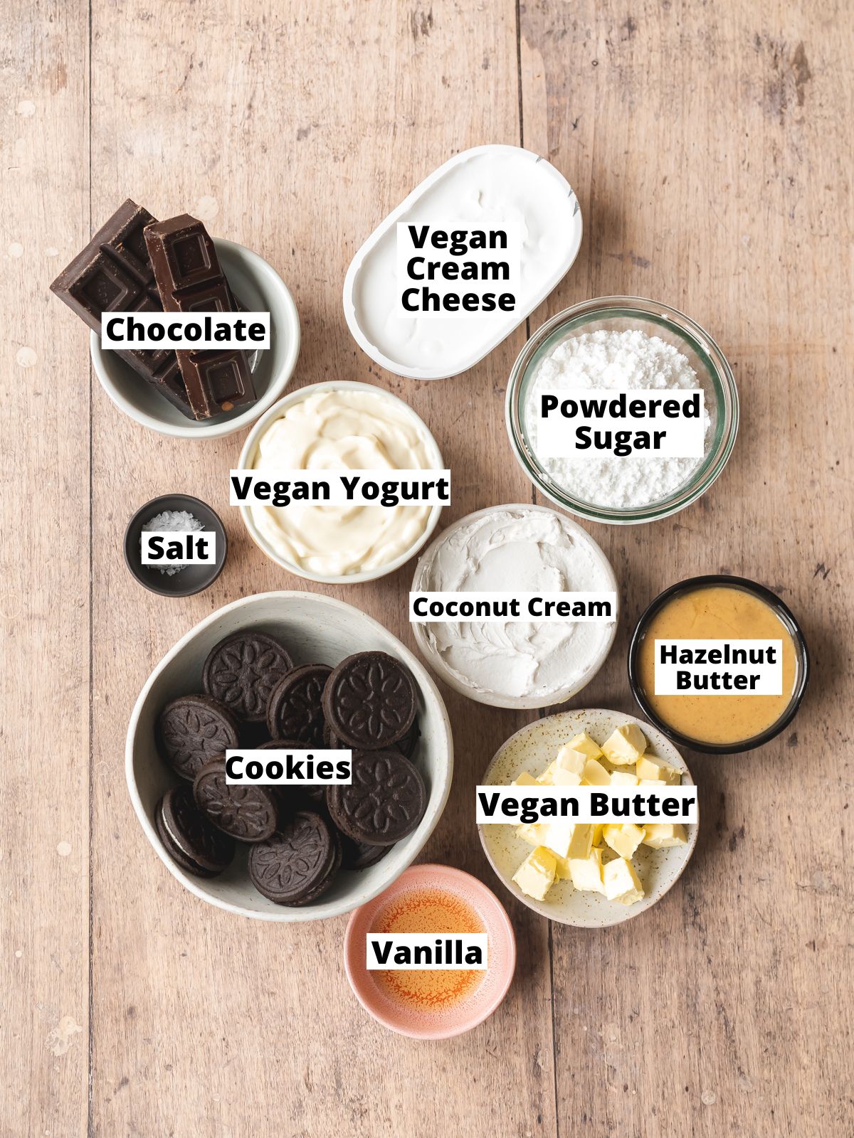 ingredients needed to make vegan no bake mini cheesecakes with an oreo cookie crust measured out into bowls on a wooden table with text overlay.