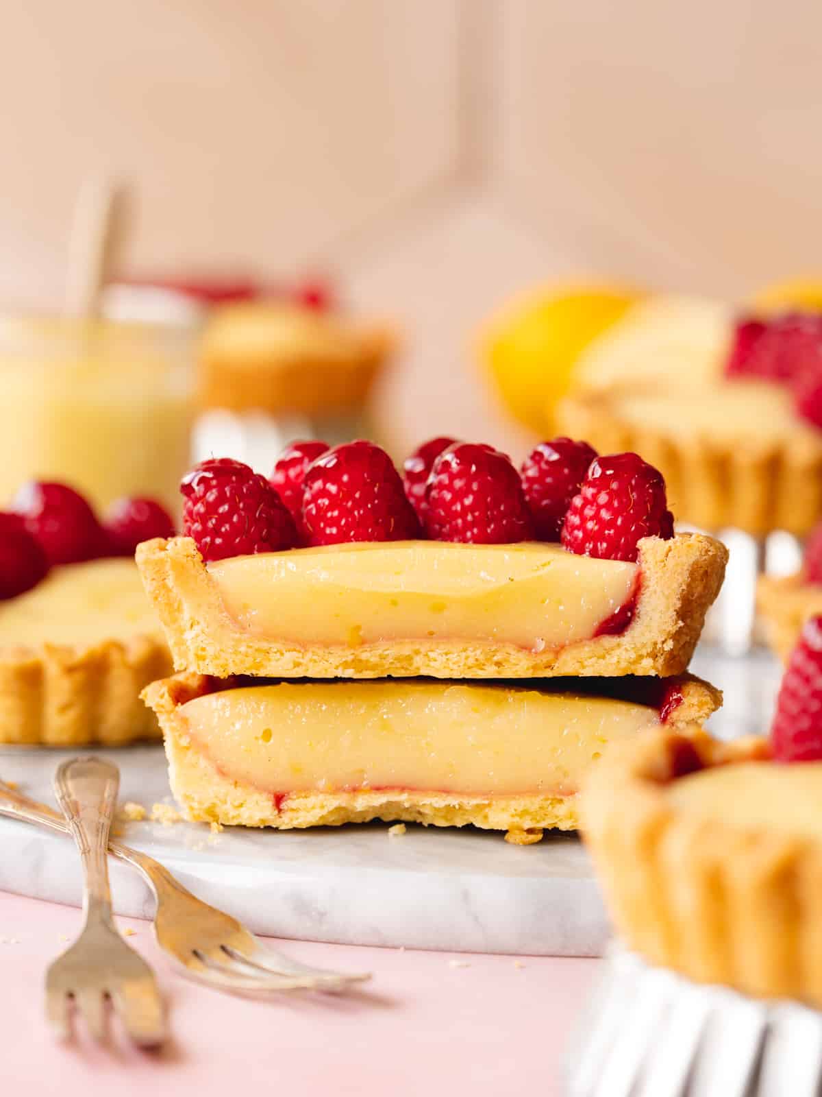 Side on shot of a halved mini lemon tart with the berry topped half stacked on top of the bare half to show the thick consistency of the lemon curd and the golden color of the vegan tart crust.