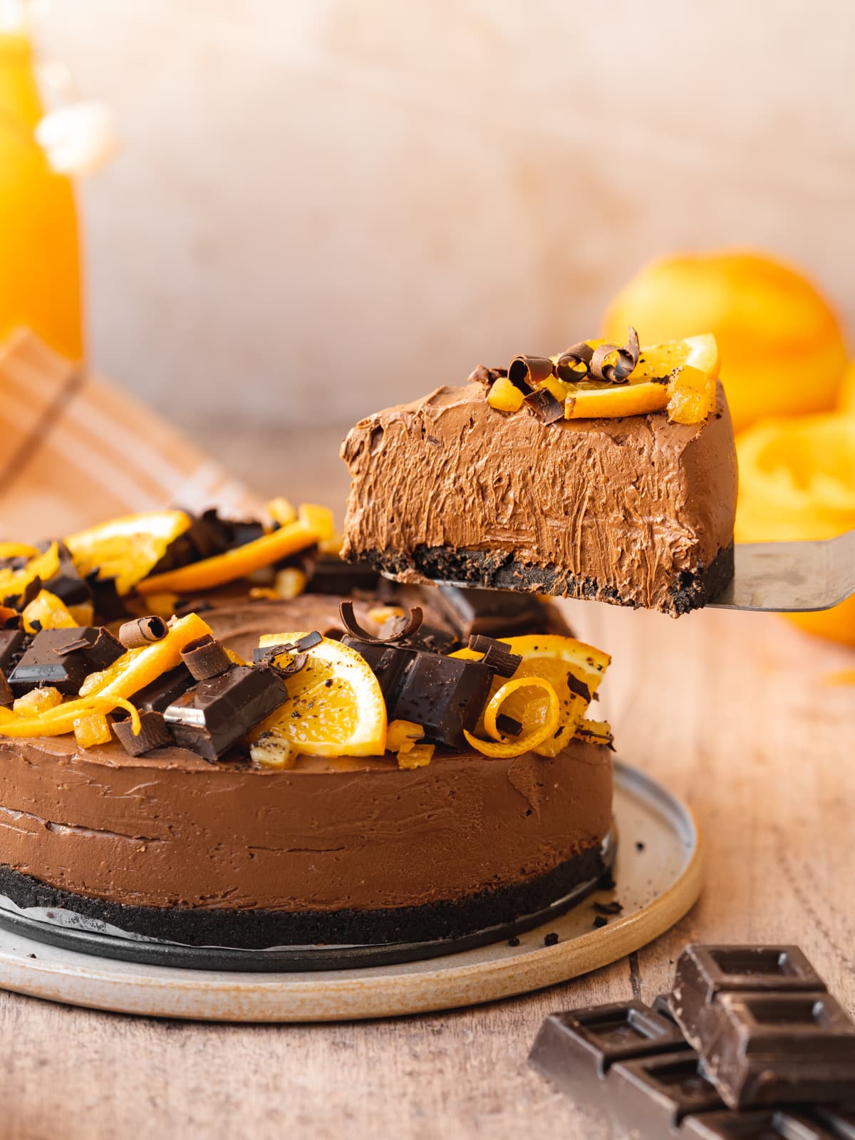 Side-on shot of a decorated orange chocolate cheesecake with a cake server removing a slice.