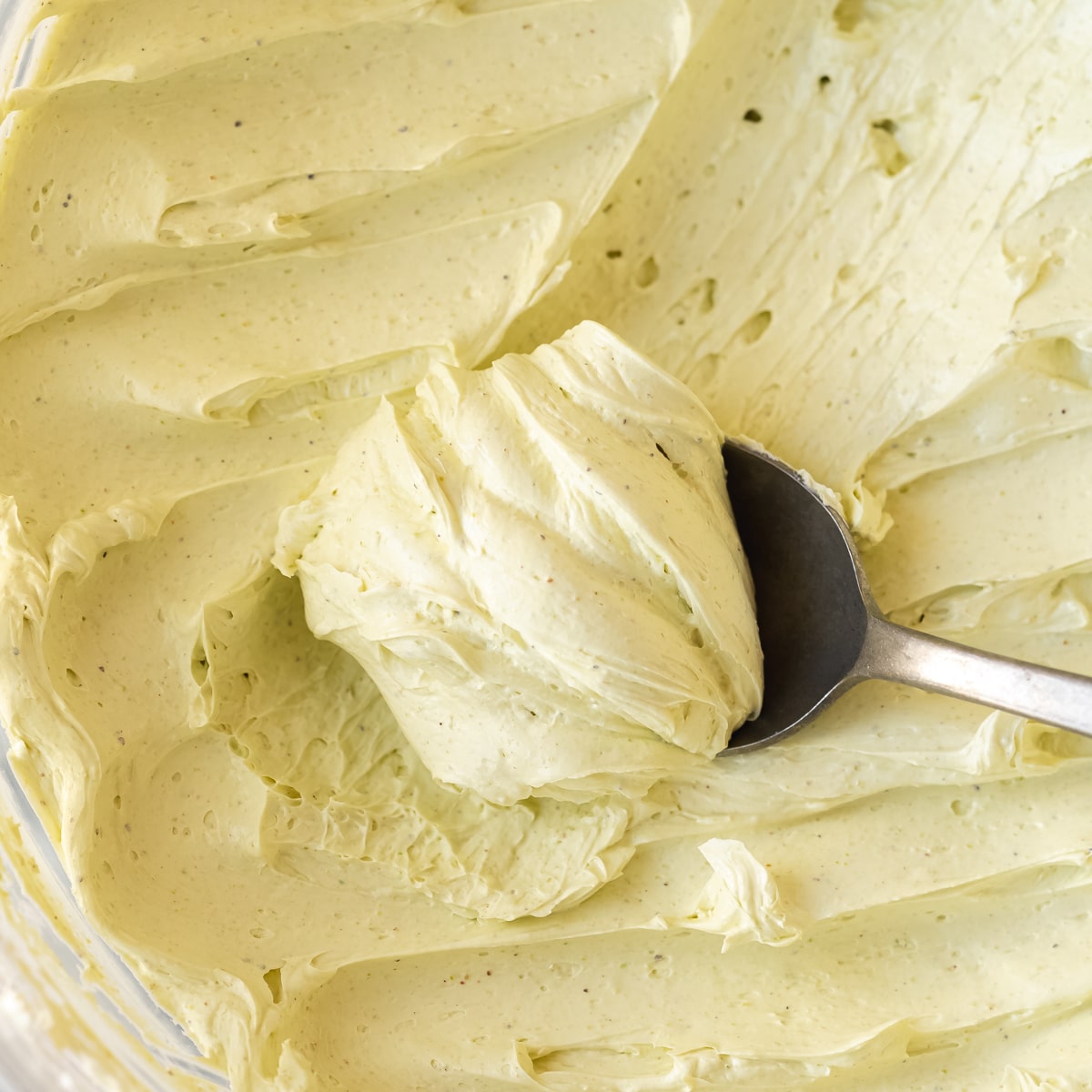 hero shot of pistachio buttercream frosting with a spoon scooping out some, showing the thick, light, airy, and creamy consistency.