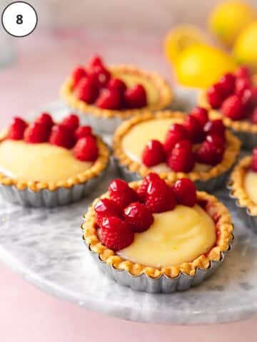 Vegan mini lemon curd tarts are topped with raspberries that have been glazed with raspberry jam for serving.