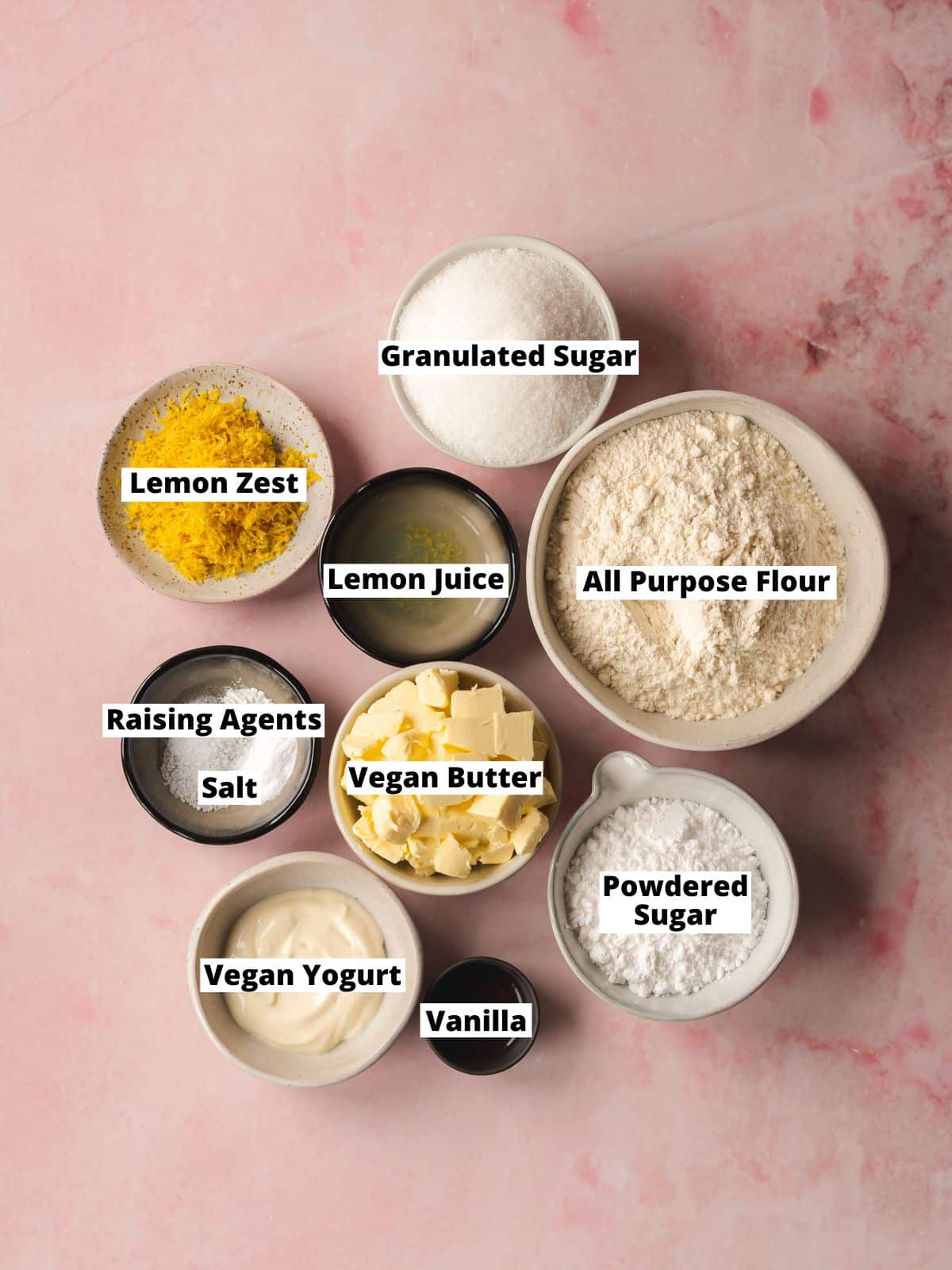 ingredients for vegan lemon cookies measured out in bowls on a marble pink surface.