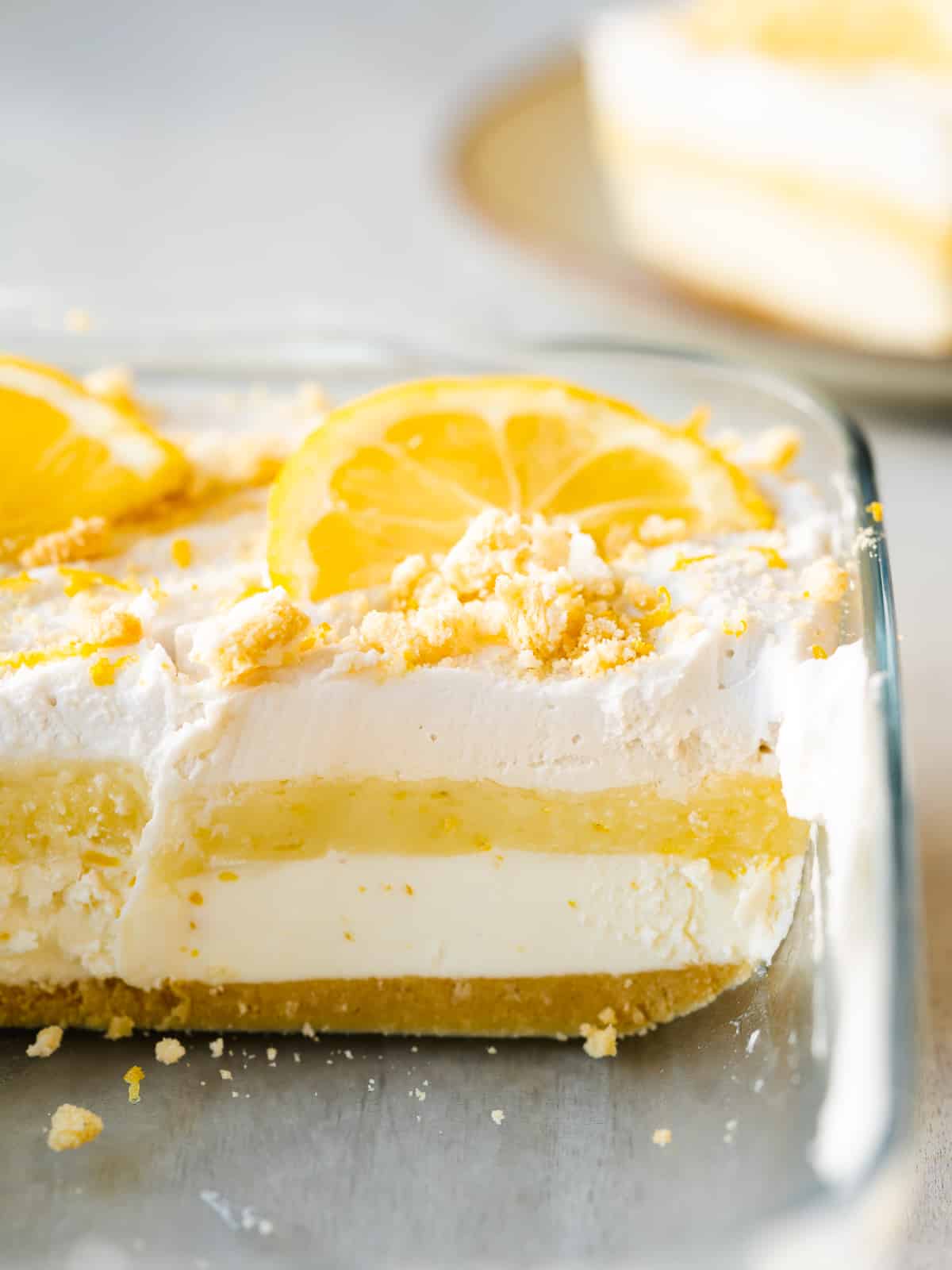 Closeup shot of completed lemon lush dessert lasagna in the baking pan with a slice removed to show the clear layers.