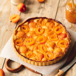 45 degree angle shot of baked vegan apricot tart with frangipane on a piece of parchment paper next to a jar of Bonne Maman preserves.