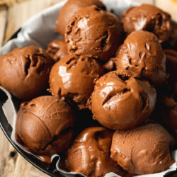 A black, parchment lined salad bowl filled to the brim with semi-melting scoops of chocolate oat milk ice cream.