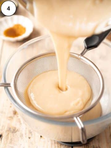 Straining the cooked custard through a mesh strainer.