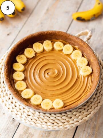 Sliced bananas being arranged in concentric circles on top of the biscoff cookie butter layer.