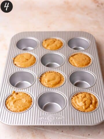 Half of the vegan pumpkin muffin batter dividied up into 6 wells of a 12-well muffin tin with spaces left between them.