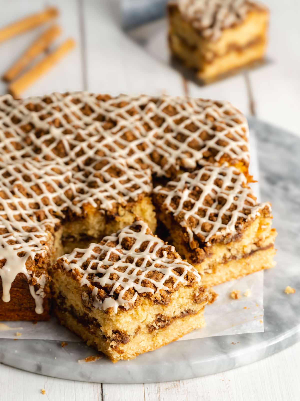 a coffee cake on a marble cutting board cut into slices with maple icing drizzled on top.