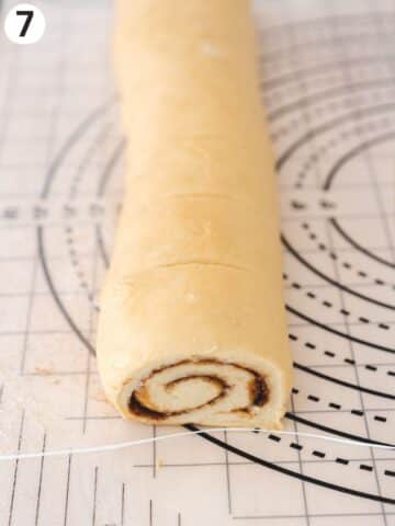 Rolled cinnamon bun baton on a working surface with measurements to cut at the right size and a piece of unflavored dental floss for cutting.
