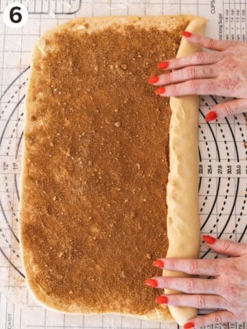 Hands rolling the vegan cinnamon roll dough along the long side to make a long tube of cinnamon buns.