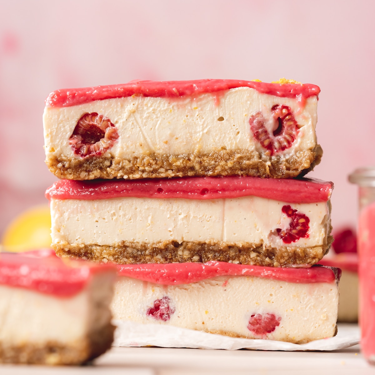 a stack of three raw lemon cheesecake bars topped with pink raspberry curd.