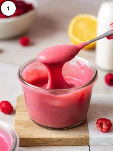 thick raspberry curd being lifted with a spoon out of a Weck jar.