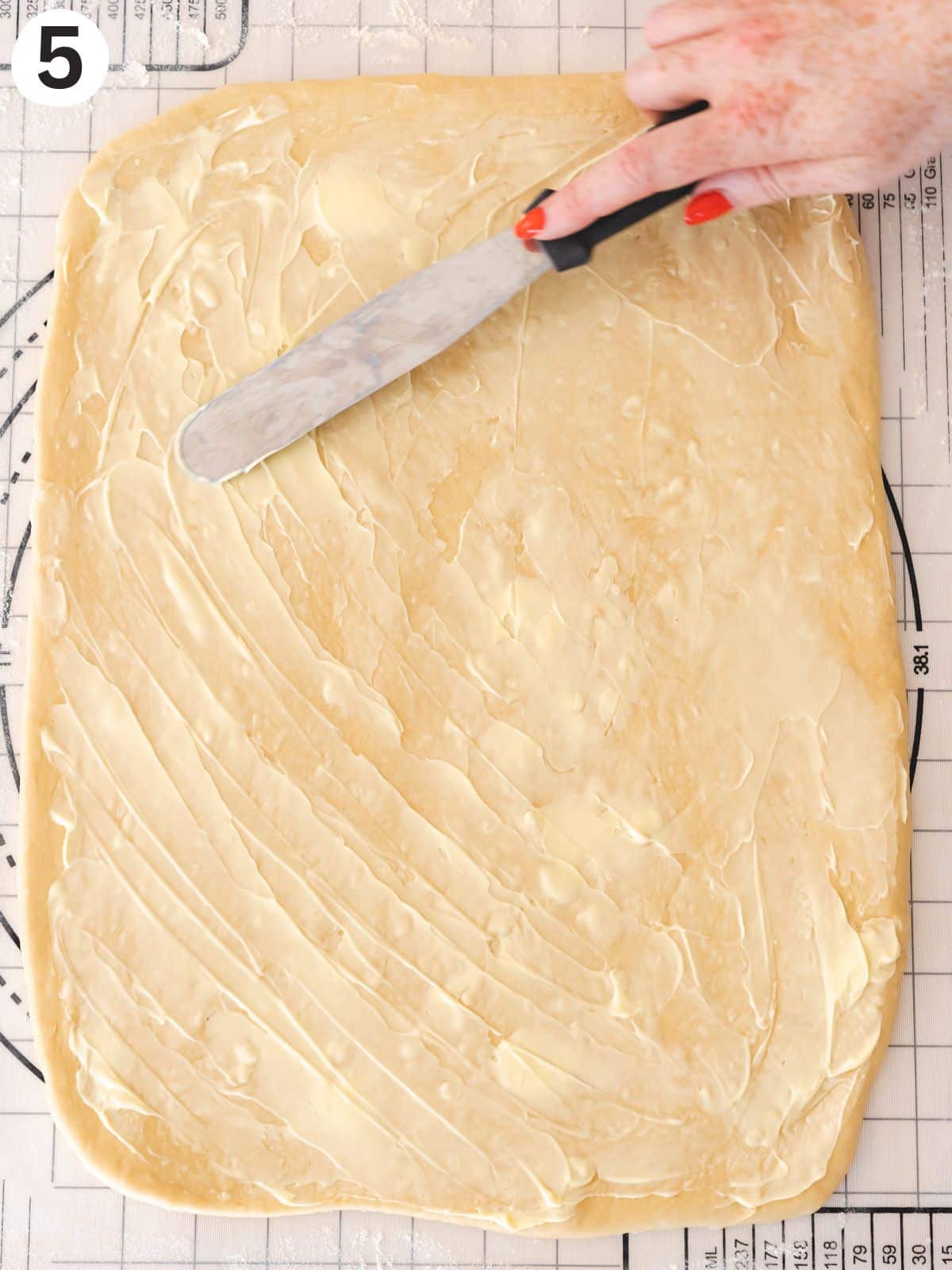 Vegan butter being spread out on the cinnamon bun dough rectangle.