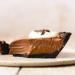 Side-on hero shot of a slice of vegan chocolate french silk pie on an earthenware dessert plate with a bite taken out to show the creamy consistency of the filling.