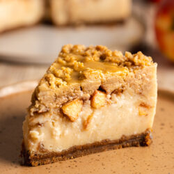 Slice of vegan apple crumble cheesecake on a speckled earthenware plate.