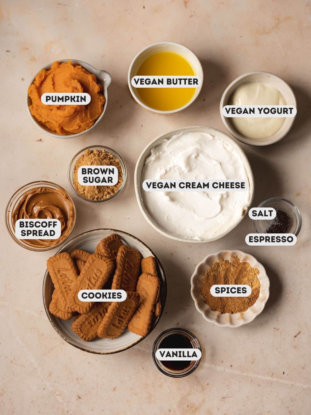 Ingredients needed to make vegan no-bake pumpkin cheesecake bars measured out into bowls on a white table.