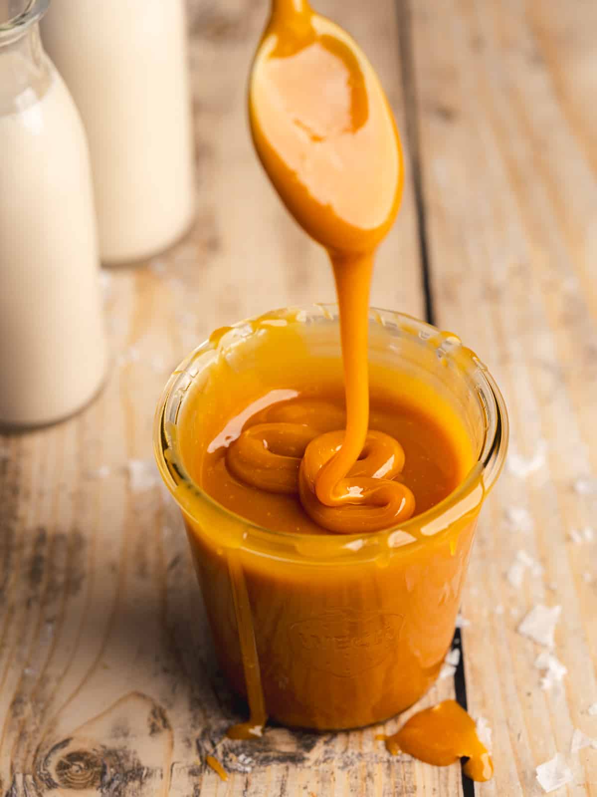 thick golden caramel sauce in a weck jar with a spoon drizzling caramel showing the silky consistency.