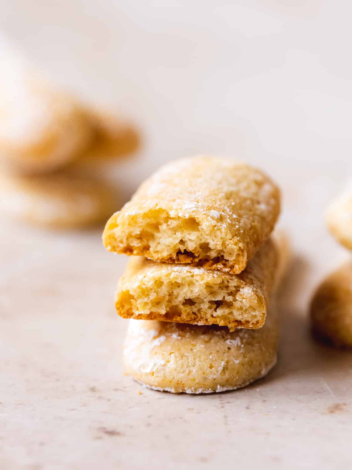 three ladyfinger cookies stacked on top of each other, with one sliced in half showing the cross-section and crunch consistency.