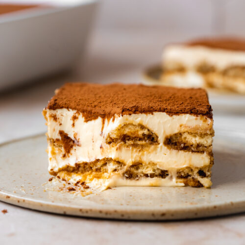 a serving of homemade tiramisu on a ceramic plate with a spoonful missing from it.