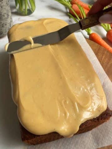 spreading brown butter icing on a loaf cake with a spatula.