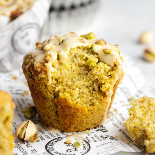 a vegan pistachio muffin with vanilla glaze and crumble topping on top of a piece of newspaper.