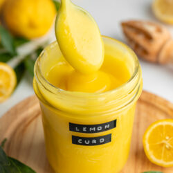 jar of lemon curd with label and lemons in the background.