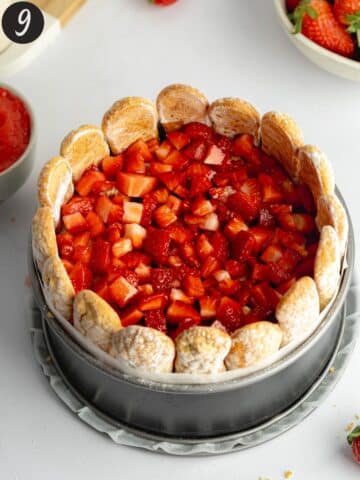 a second layer of strawberry pieces added on top of ladyfingers in a cake pan.