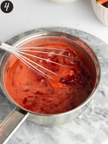strawberry curd in a saucepan with cornstarch being whisked in to thicken it.