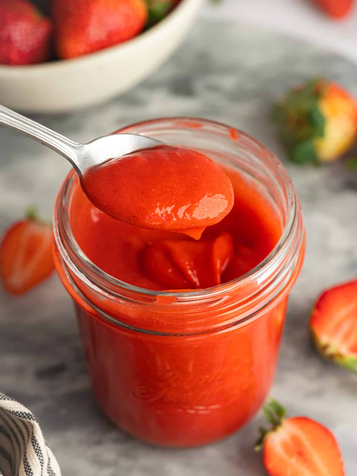 a spoon lifting out a spoonful of thick strawberry curd from a jar.
