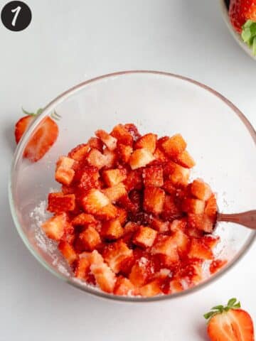strawberries and sugar macerating in a clear bowl.