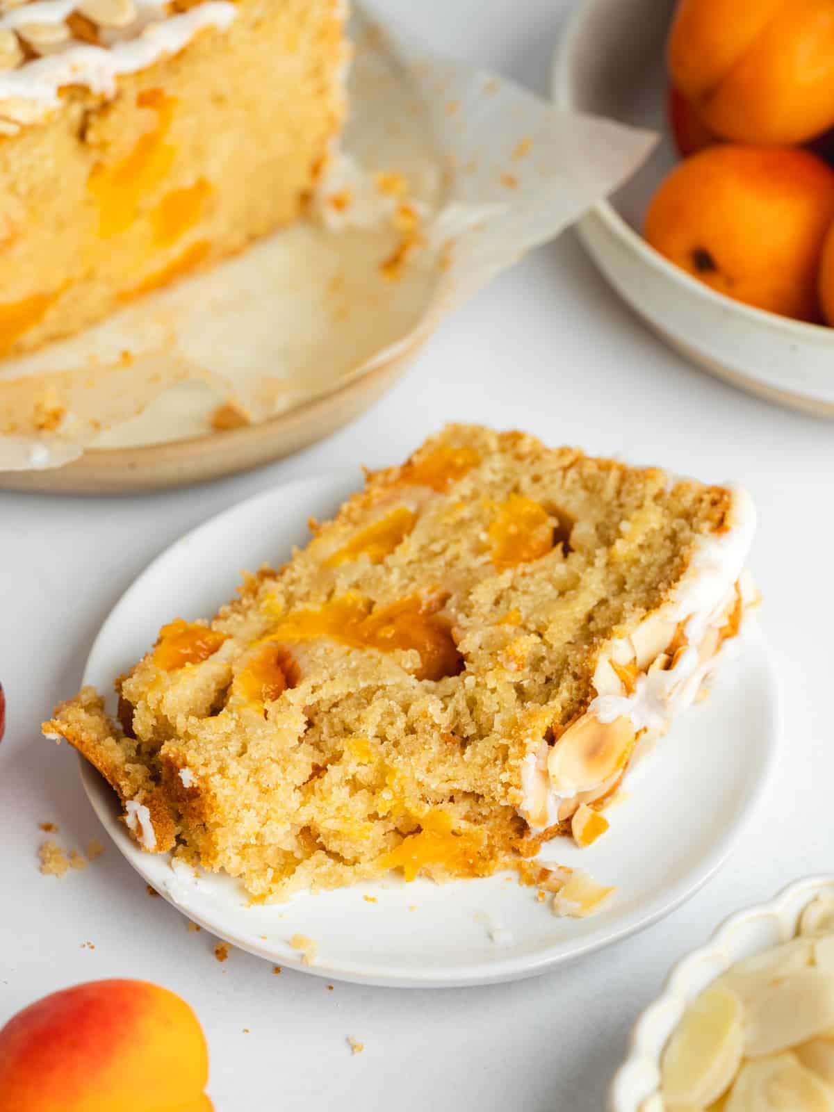 a slice of apricot cake with a piece missing on a white plate.