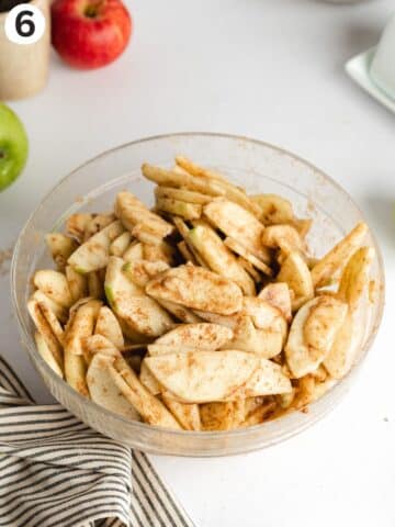 a mixing bowl with apple slices coated in cinnamon, flour and vanilla.