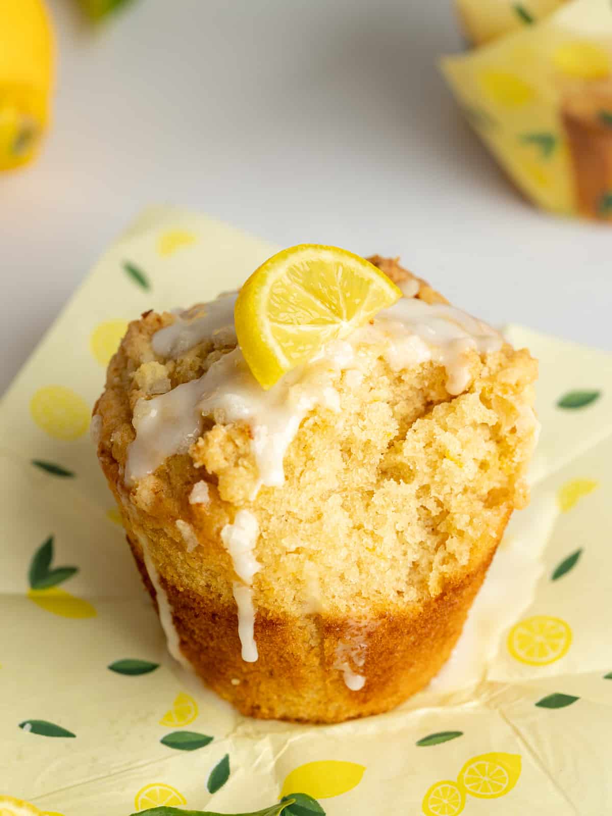 a lemon muffin with crumble topping and a bit taken out of it revealing the fluffy interior.