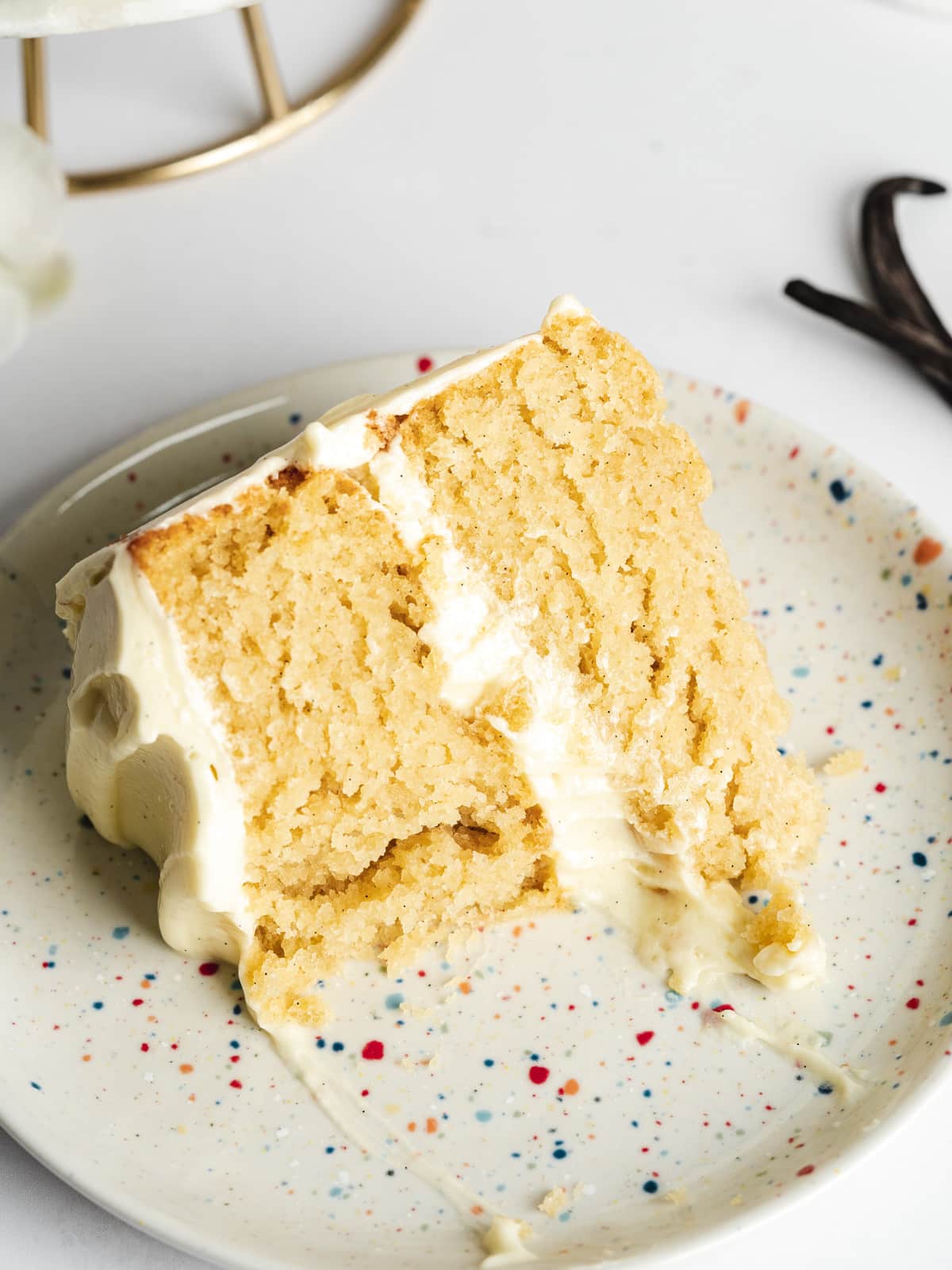 a slice of vegan vanilla cake on a speckled plate with a forkful taken from it showing the moist and tender crumb.